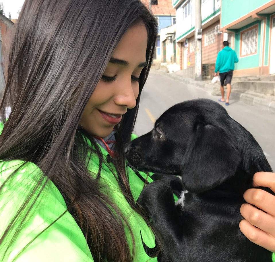 Voluntaria de Arca Luminosa cargando a un cachorro negro rescatado en una calle de Bogotá
